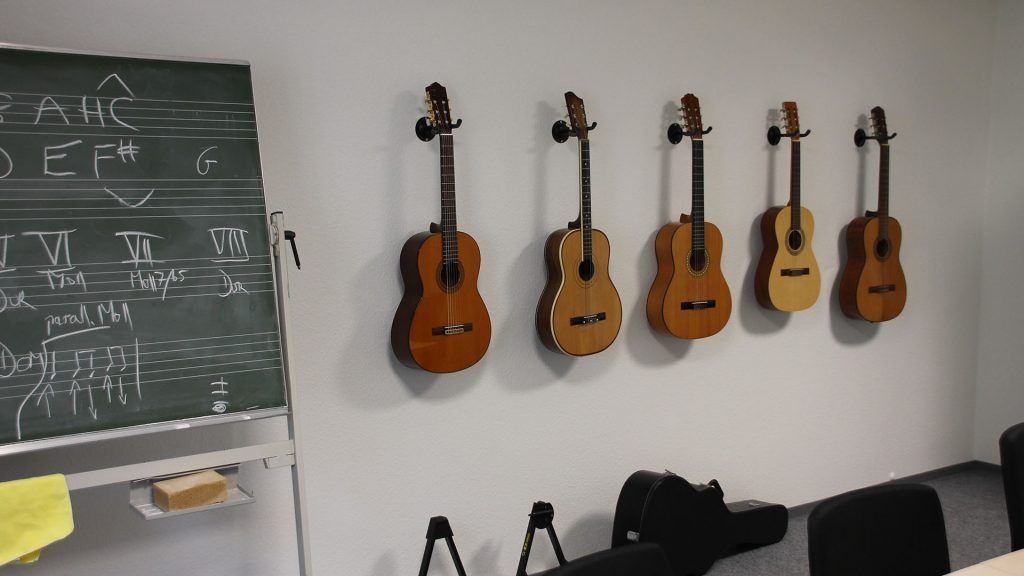 Ein Raum mit einer Kreidetafel auf der Noten stehen. An einer Wand hängen zahlreiche Gitarren.
