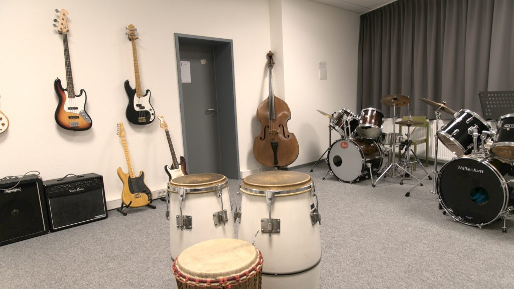 Ein Raum mit unterschiedlichen Musikinstrumenten. Zu sehen sind Gitarren, ein Schlagzeug und ein Kontrabass.